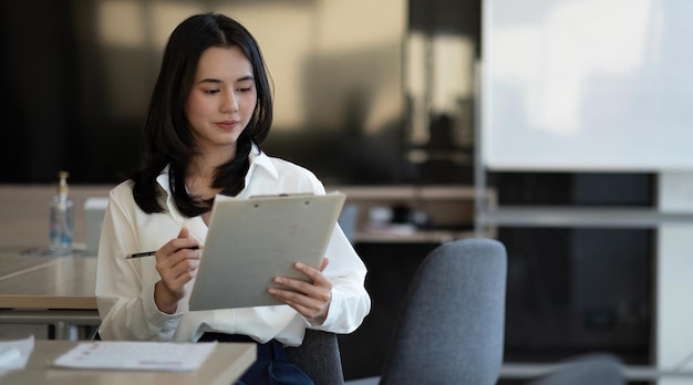 Retrato de una exitosa joven empresaria asiática que trabaja con un informe financiero en su oficina.