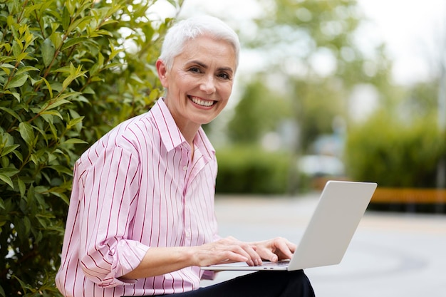 Foto retrato de una exitosa mujer de negocios senior usando una computadora portátil sentada en un banco al aire libre