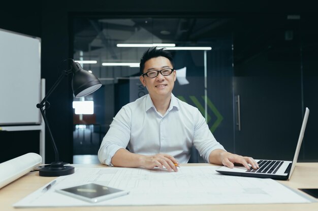 Retrato de un exitoso arquitecto masculino asiático sonriendo y mirando la cámara trabajando en el plan del proyecto