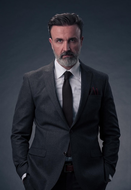 Retrato de un exitoso y elegante hombre de negocios de alto nivel con barba gris y ropa informal de negocios confiado en un estudio fotográfico aislado en un fondo oscuro gesticulando con las manos. foto de alta calidad