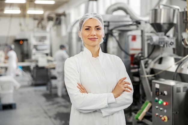 Retrato de un exitoso gerente de fábrica de alimentos en uniforme estéril con los brazos cruzados sonriendo