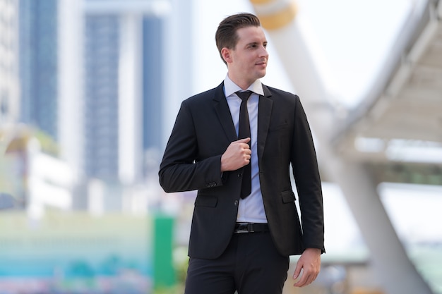 Retrato de exitoso hombre de negocios de pie frente a modernos edificios de oficinas