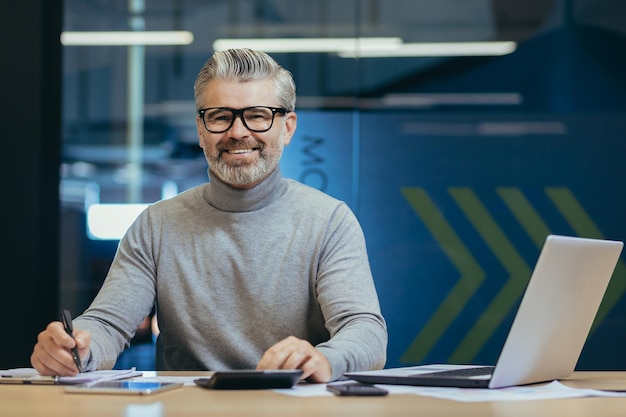 Retrato de un exitoso hombre de negocios senior de cabello gris con gafas sonriendo y mirando a la cámara