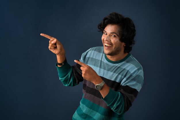 Retrato de un exitoso joven alegre señalando y presentando algo con la mano o el dedo con una cara sonriente feliz