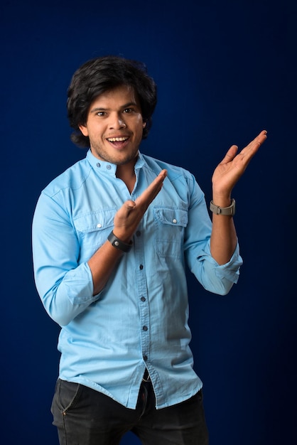 Retrato de un exitoso joven alegre señalando y presentando algo con la mano o el dedo con una cara sonriente feliz