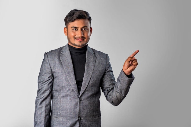 Retrato de un exitoso joven alegre con traje formal que señala y presenta algo con la mano o el dedo con una cara sonriente feliz