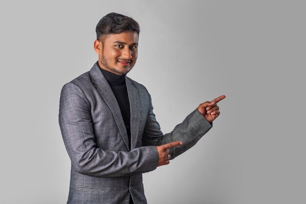 Retrato de un exitoso joven alegre con traje formal que señala y presenta algo con la mano o el dedo con una cara sonriente feliz