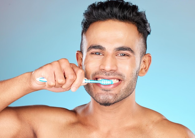 Retrato facial dental e homem escovando os dentes no estúdio isolado em um fundo azul Saúde bucal de bem-estar e rotina do modelo masculino feliz segurando a escova de dentes para higiene oral e atendimento odontológico