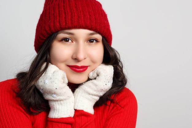 Retrato facial de linda mujer joven feliz con suéter y sombrero de punto rojo sobre fondo blanco.