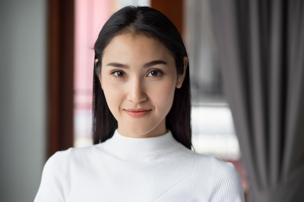 Retrato facial de mujer asiática sonriente feliz retrato de mujer asiática sonriente feliz segura de sí misma sonríe en un entorno interior urbano modelo de mujer asiática china adulta joven