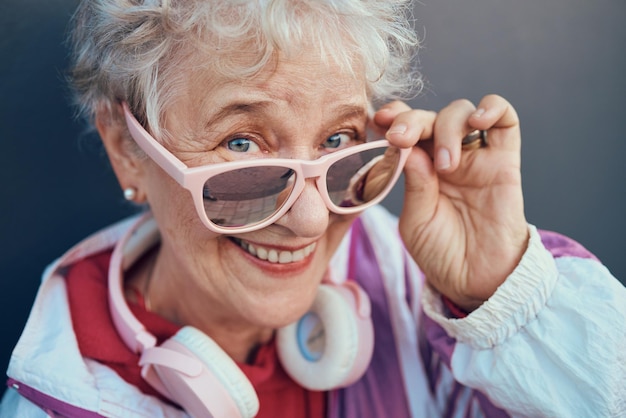 Retrato facial y mujer mayor con gafas de sol, auriculares y ropa vintage Belleza de la moda y feliz mujer jubilada y anciana con gafas retro de diseño fresco y rosa y ropa con sonrisa