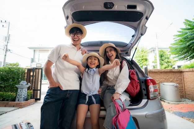 Retrato de familia asiática con padre, madre e hija se ve feliz mientras prepara la maleta en un coche para vacaciones.