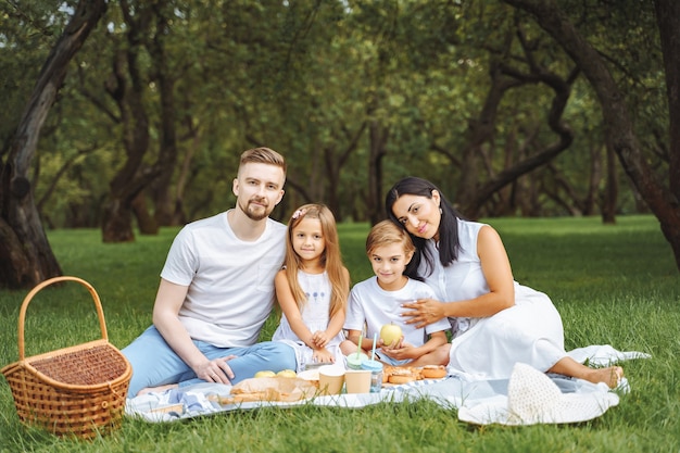 Retrato de una familia feliz abrazándose y mirando a la cámara mientras se relaja en el césped durante un picnic