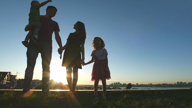 Retrato de familia feliz al atardecer - padre, madre, hija e hijo pequeño - silueta, tiro de teleobjetivo