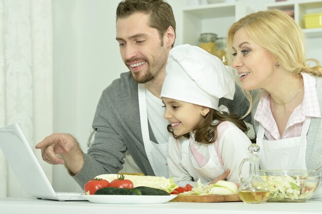 Retrato de familia feliz cocinando en la cocina con un portátil