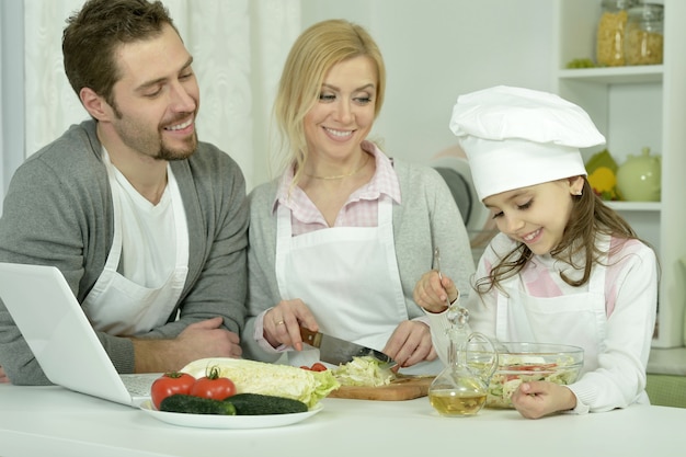 Retrato de familia feliz cocinando en la cocina con un portátil