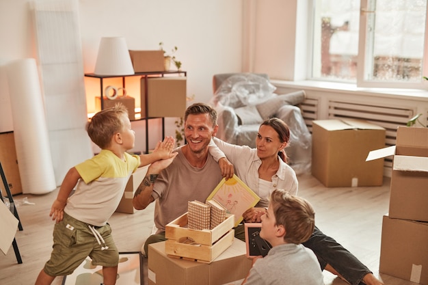 Retrato de familia feliz con dos hijos desempacando cajas mientras celebra la mudanza a la nueva copia de hogar ...