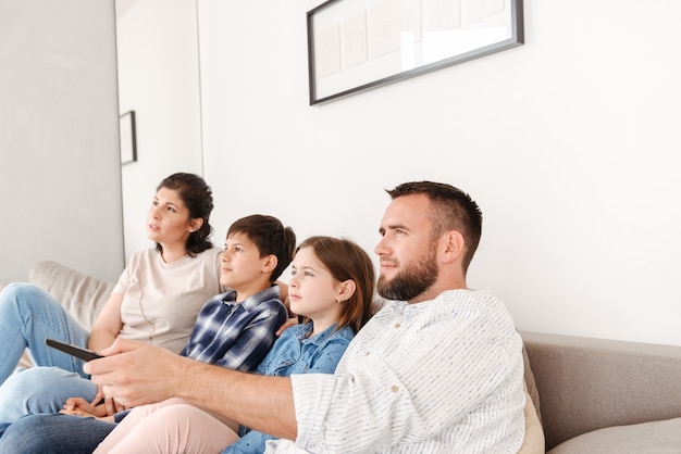 Retrato de familia feliz con dos niños descansando en la sala de estar en casa y sentados juntos en el sofá mientras ven la televisión