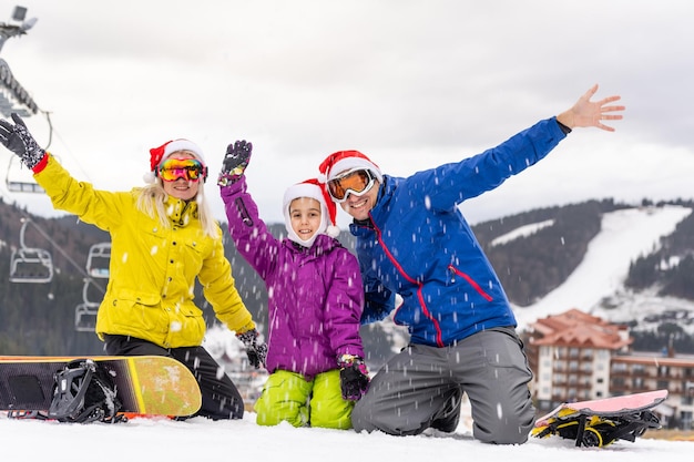 Retrato de familia feliz en gorros de Santa y snowboard en el resort de invierno