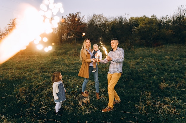 Retrato de una familia feliz con luces de Bengala en un campo verde al atardecer