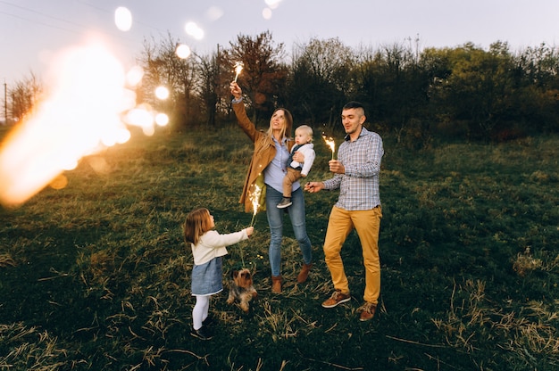 Foto retrato de una familia feliz con luces de bengala en un campo verde al atardecer