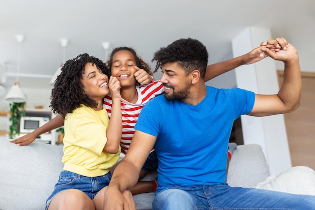 Retrato de familia feliz Madre feliz padre y su hija linda posando en la sala de estar en casa Niña pequeña sentada en los hombros de papá espacio libre