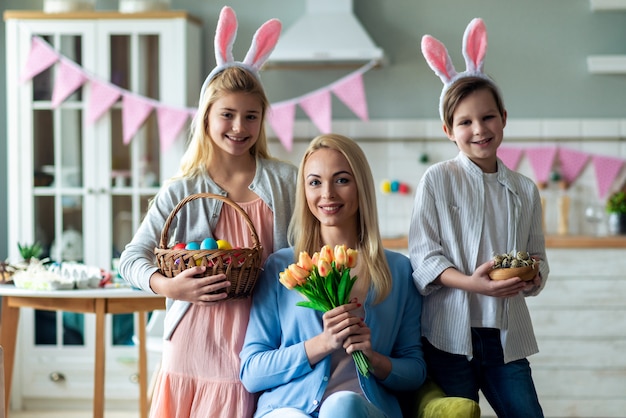 Retrato de familia feliz. Madre sentada y sosteniendo un ramo de tulipanes, hijo e hija están sosteniendo una canasta con huevos de Pascua.