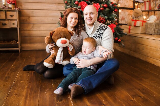 Retrato de familia feliz en Navidad, madre, padre e hijo sentados en una silla alta en casa, decoración navideña y regalos a su alrededor