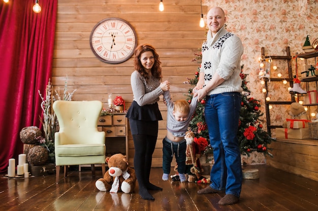 Retrato de familia feliz en Navidad, madre, padre e hijo sentados en una silla alta en casa, decoración navideña y regalos a su alrededor