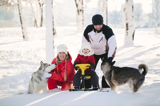 Retrato de una familia feliz en un parque de invierno Papá mamá hijo y perros posan en la nieve en un día soleado