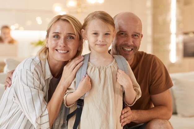 Retrato de familia feliz sonriendo mientras posa con linda niña con mochila