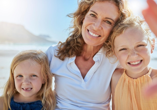 Retrato de una familia feliz tomándose una selfie en la playa mientras estaba de vacaciones en verano Mujer madura pasando tiempo de calidad con niños adoptados o de acogida Niñas pequeñas de excursión con su abuela