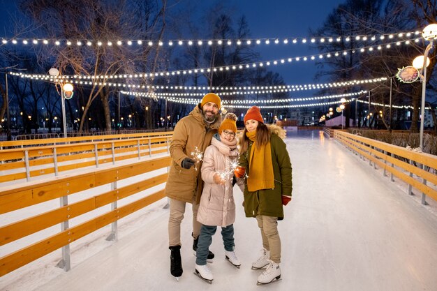 Retrato de familia feliz de tres con estrellitas de pie sobre la pista de hielo al aire libre durante las vacaciones de Navidad