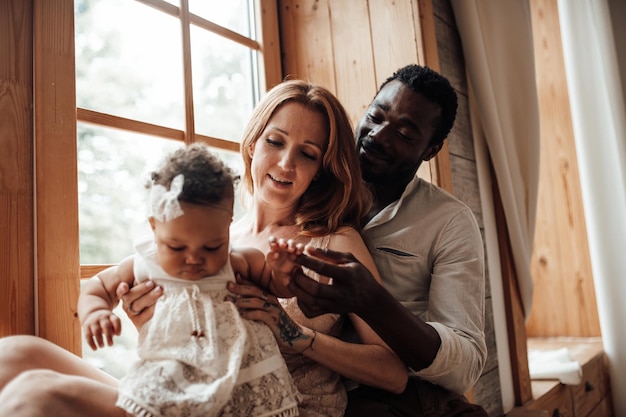 Retrato de una familia interracial feliz y amistosa con un bebé moreno junto a la ventana