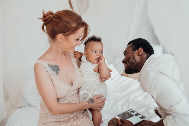 Retrato de una familia interracial feliz y amistosa con un bebé moreno juntos en un dormitorio acogedor