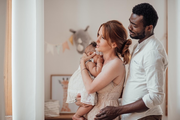 Retrato de una familia interracial feliz y amistosa con un bebé moreno juntos en la habitación de los niños