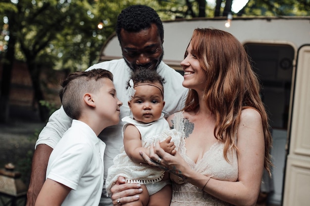 Retrato de una familia interracial feliz y amistosa con dos niños al aire libre cerca del remolque de viaje retro