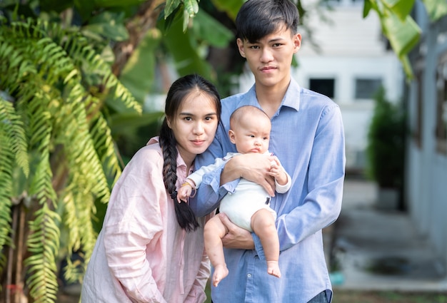 Retrato de la familia joven asiática feliz que se coloca al aire libre con sonrisa y amor, día de la madre y concepto del padre.