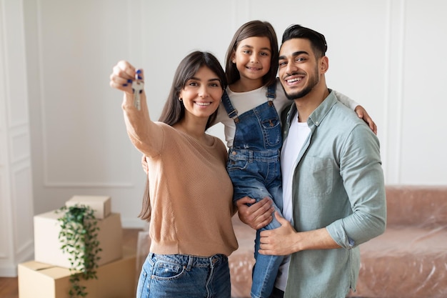 Retrato de familia joven feliz mostrando clave, padres alegres abrazando al niño pequeño, sosteniendo a la hija en las manos. Personas sonrientes que se mueven en el nuevo apartamento de pie en la sala de estar. Enfoque selectivo