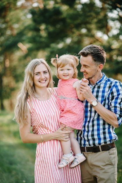 Retrato de una familia joven feliz pasar tiempo juntos en la naturaleza, de vacaciones, al aire libre. Mamá, papá e hija están parados en la hierba verde. El concepto de vacaciones en familia.