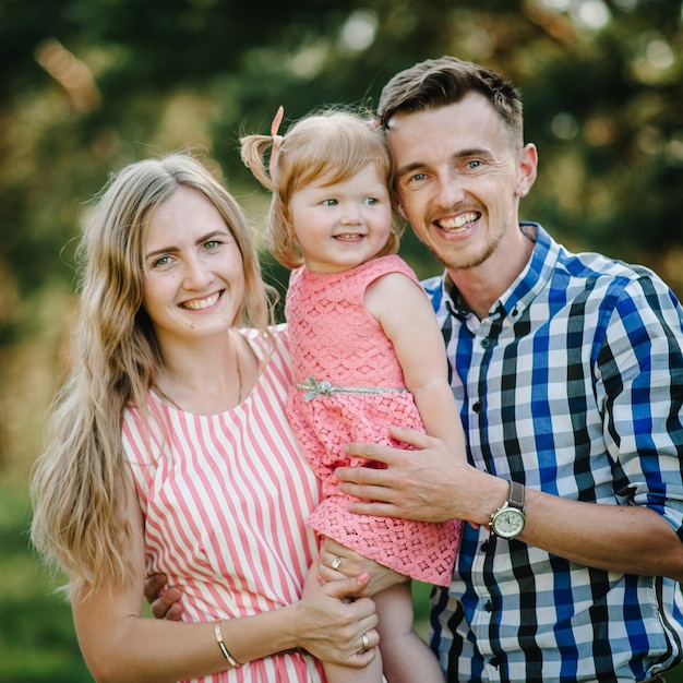 Retrato de una familia joven feliz pasar tiempo juntos en la naturaleza en las vacaciones de verano. El padre, la madre y la niña caminando y jugando en el parque a la hora del atardecer. De cerca.