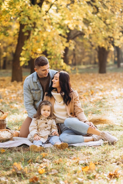 Retrato de familia joven feliz sentados en plaid juntos en el parque de otoño
