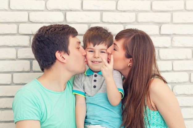 Retrato de familia joven feliz y sonriente sobre fondo de pared de ladrillo Padre y madre con niño pequeño Padres con niño