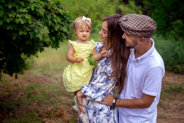 Retrato de familia joven hermosa que lleva a la pequeña niña con estilo en el parque verde en un día caluroso de verano de cerca