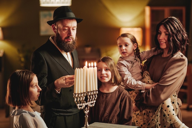 Retrato de una familia judía feliz encendiendo velas menorah durante la celebración de hanukkah en un hogar acogedor