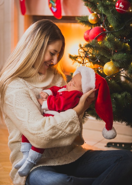 Retrato de familia de la madre y el bebé sentado en la chimenea de Navidad