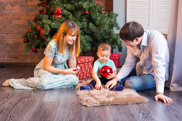 Retrato de familia de Navidad en la sala de estar de vacaciones en casa, niños y bebé en Santa Hat con caja de regalo actual, decoración de la casa con guirnalda de velas de árbol de Navidad