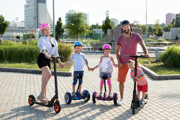 Retrato de familia con niños en scooters eléctricos y gyro scooter en el parque en verano.