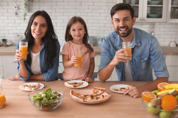 Retrato de familia sonriente sosteniendo vasos con jugo de naranja y mirando a la cámara