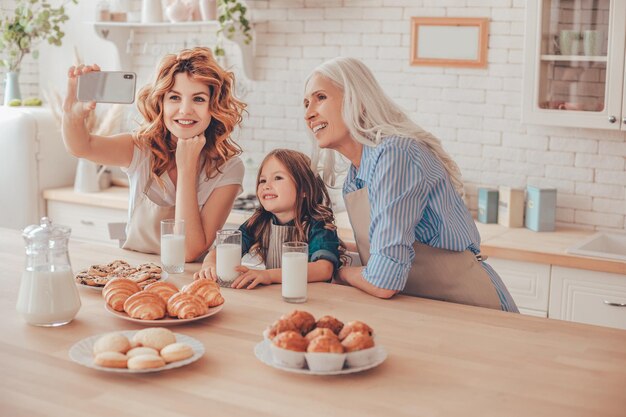 Retrato de familia sonriente tomando selfie en smartphone sentado en la cocina